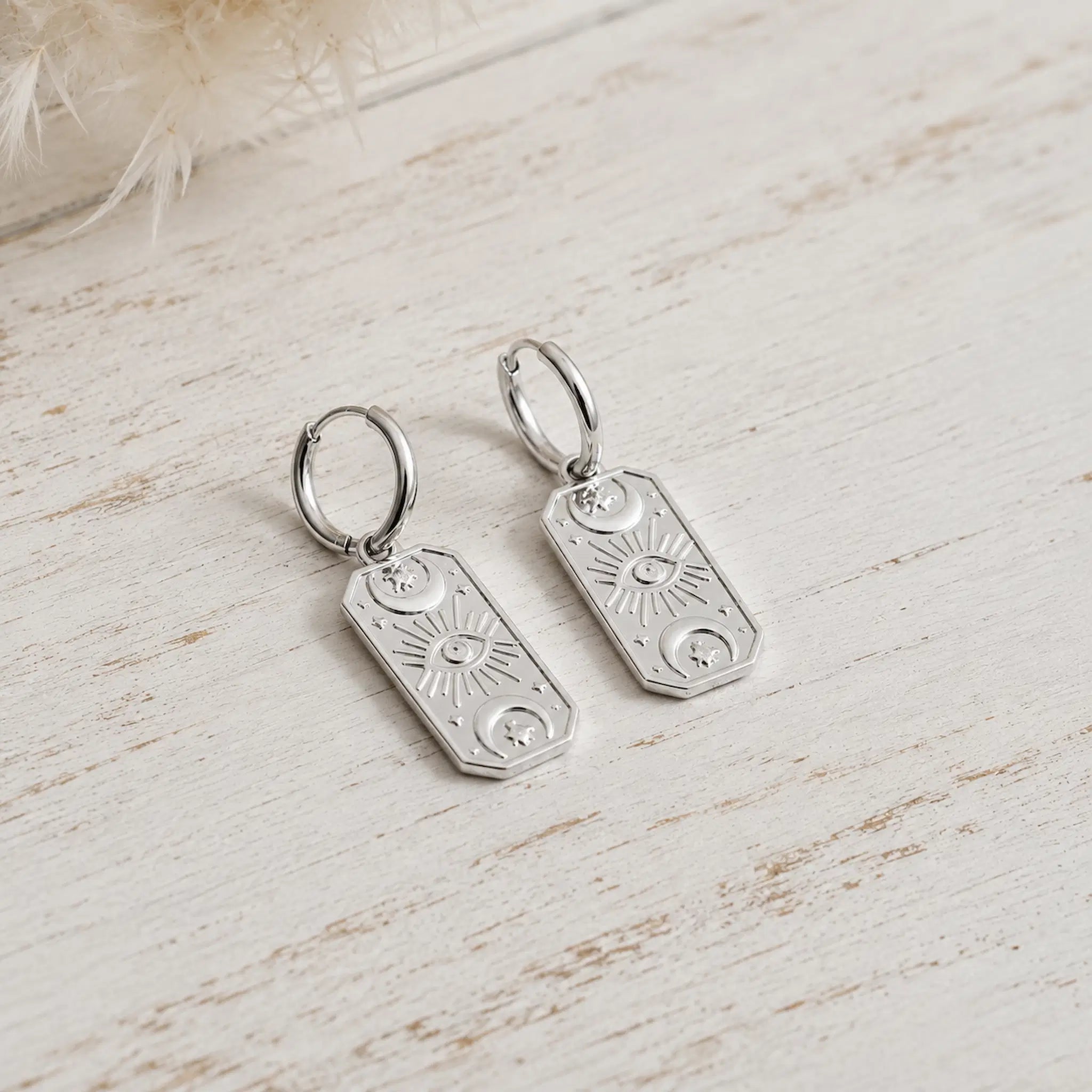 silver hoop earrings with rectangle charms with celestial design on a rustic wooden surface