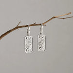 pair of silver hoop earrings hanging from a branch with rectangle shape charms with celestial design