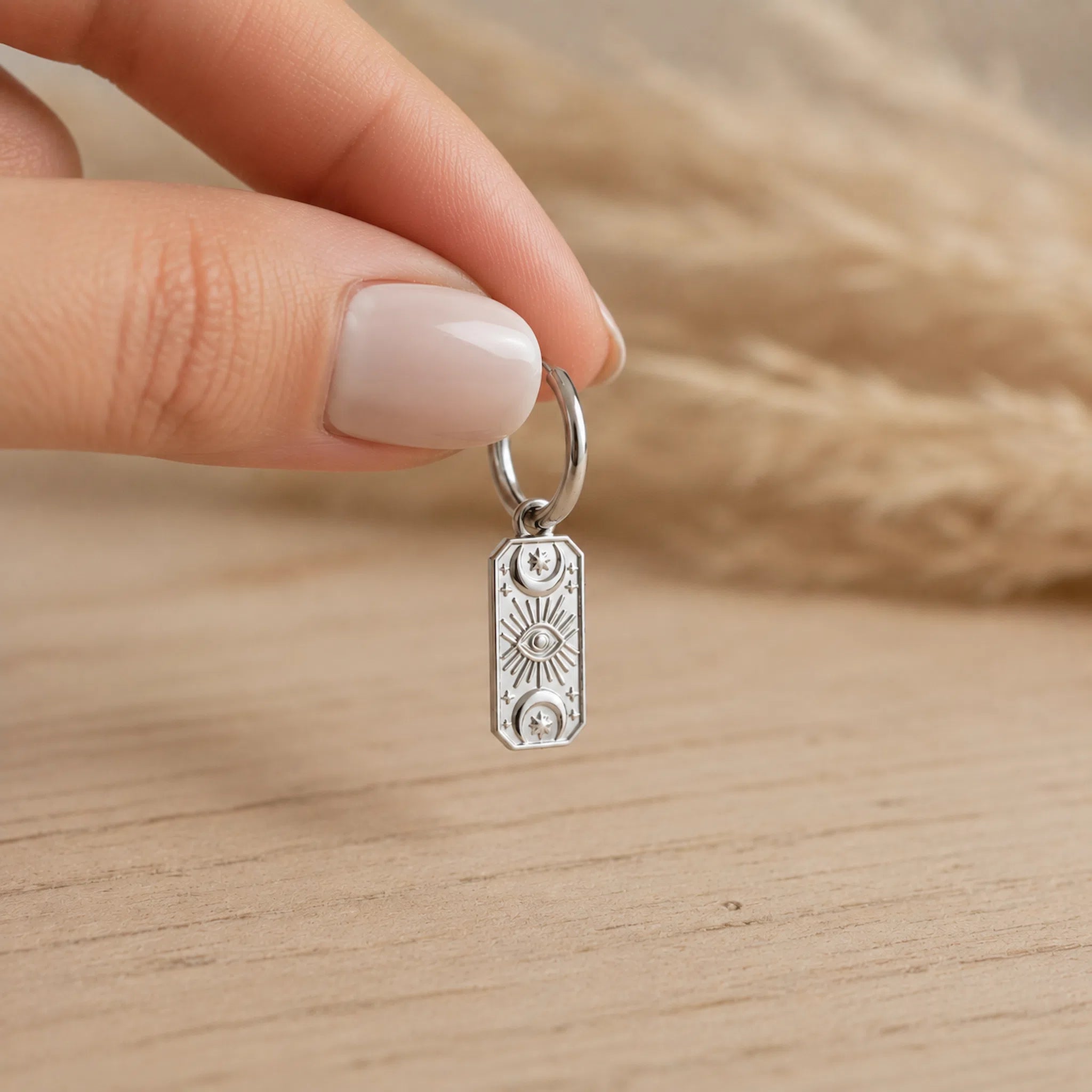 fingers holding one silver celestial charm hoop earring above a light wooden surface