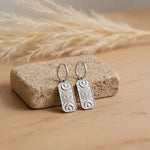 pair of silver celestial charm hoop earrings resting on a natural stone