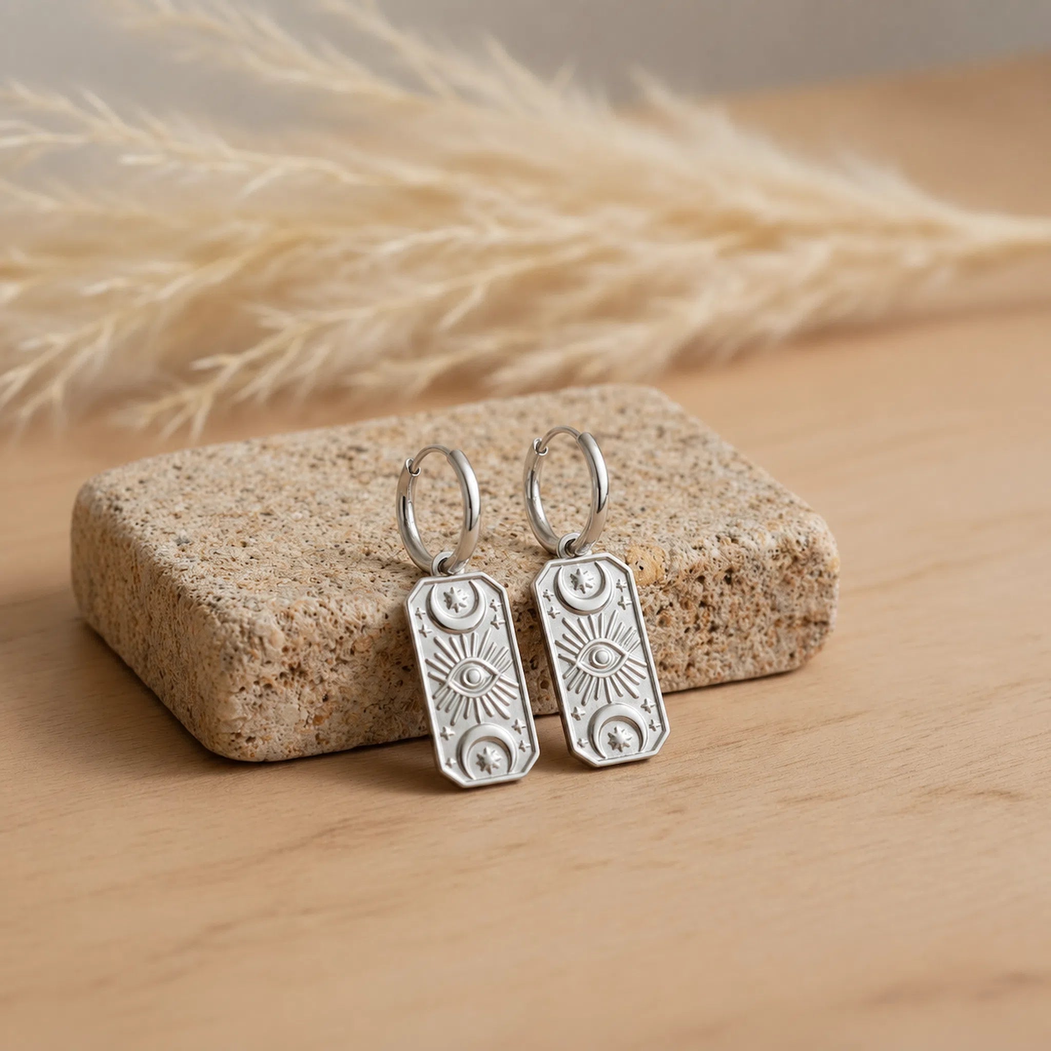 pair of silver celestial charm hoop earrings resting on a natural stone