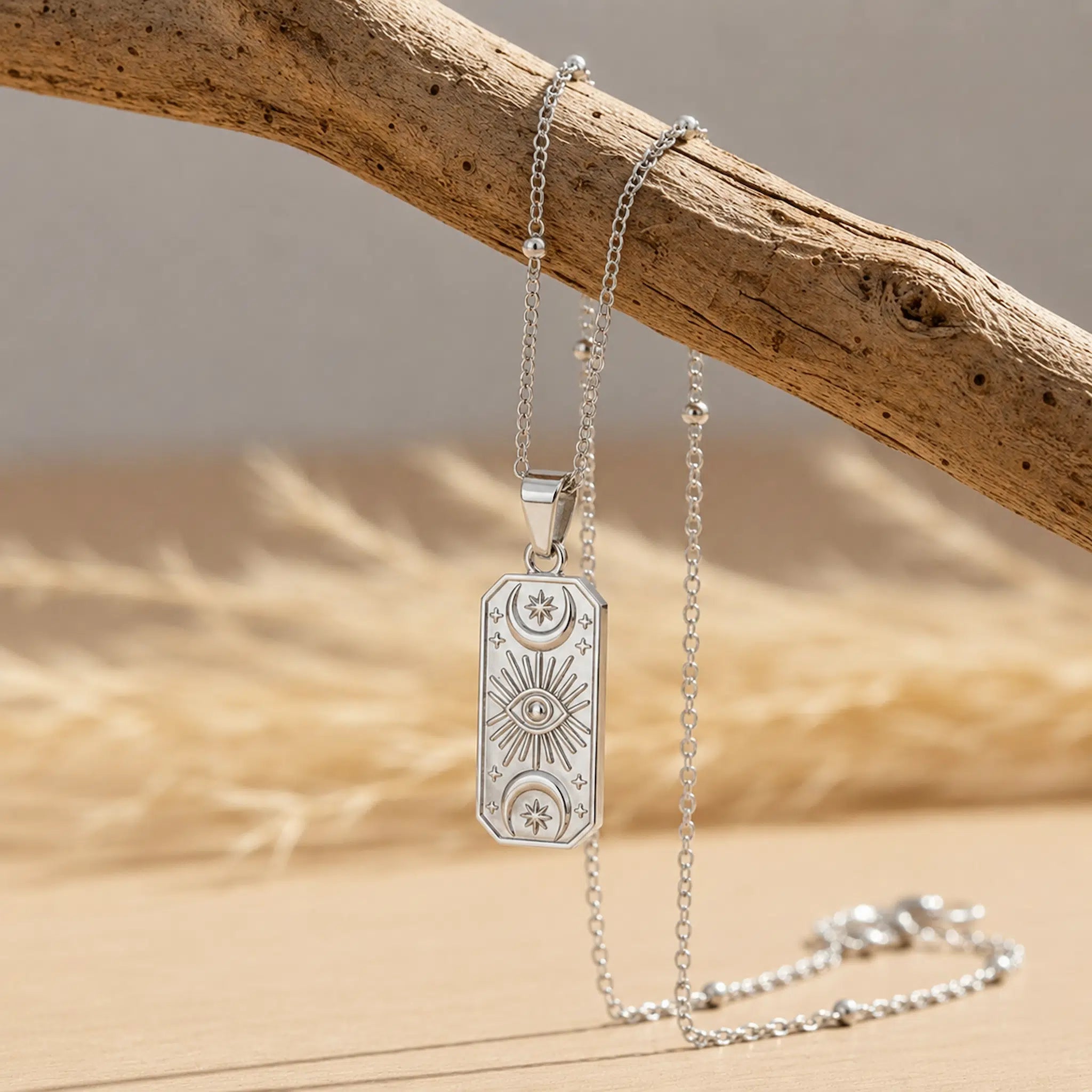 Pendant necklace by Indie and Harper: silver celestial charm on a delicate chain draped over a weathered wooden branch.