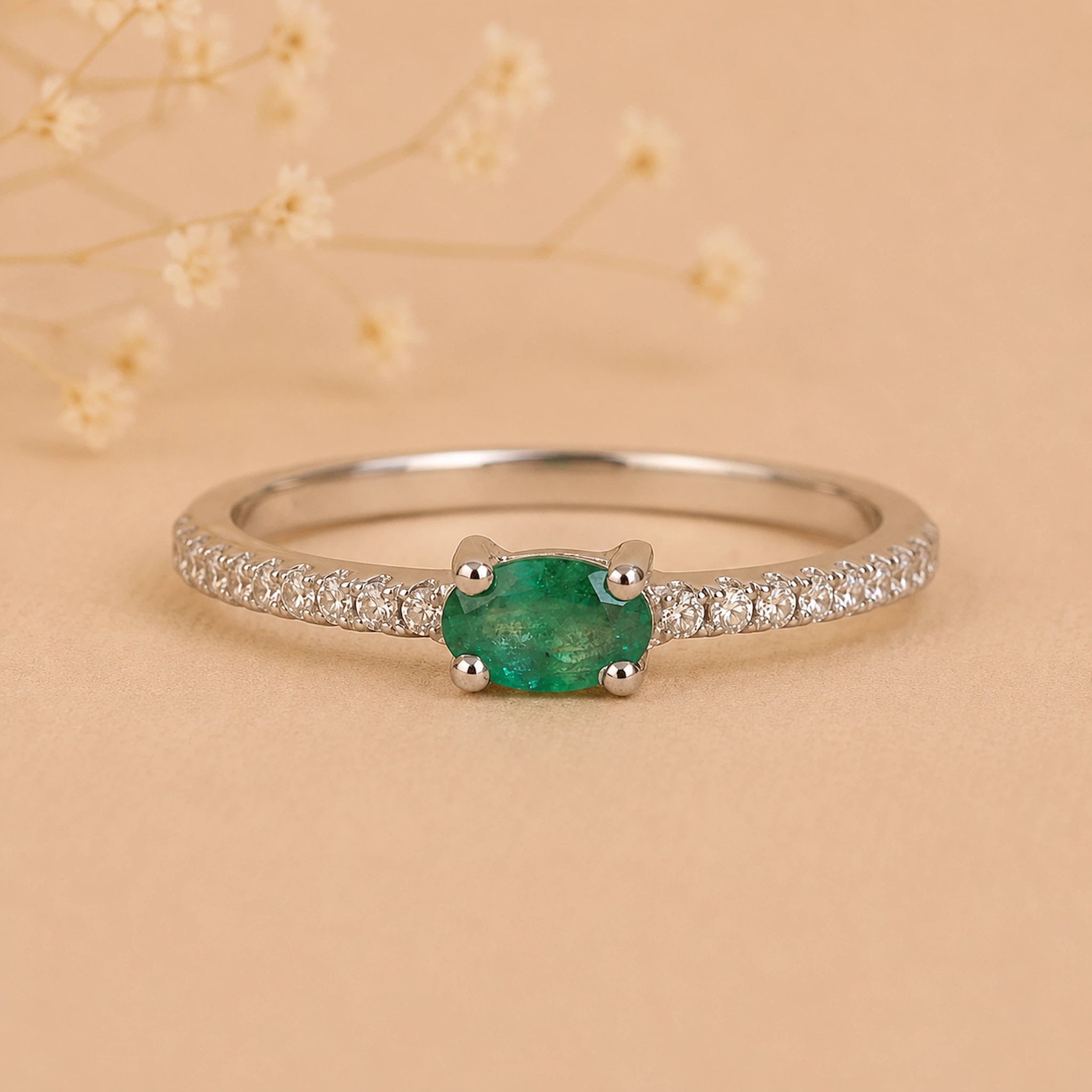 Sterling Silver Pave Ring with a oval shaped green faceted claw set emerald gemstone on a beige background