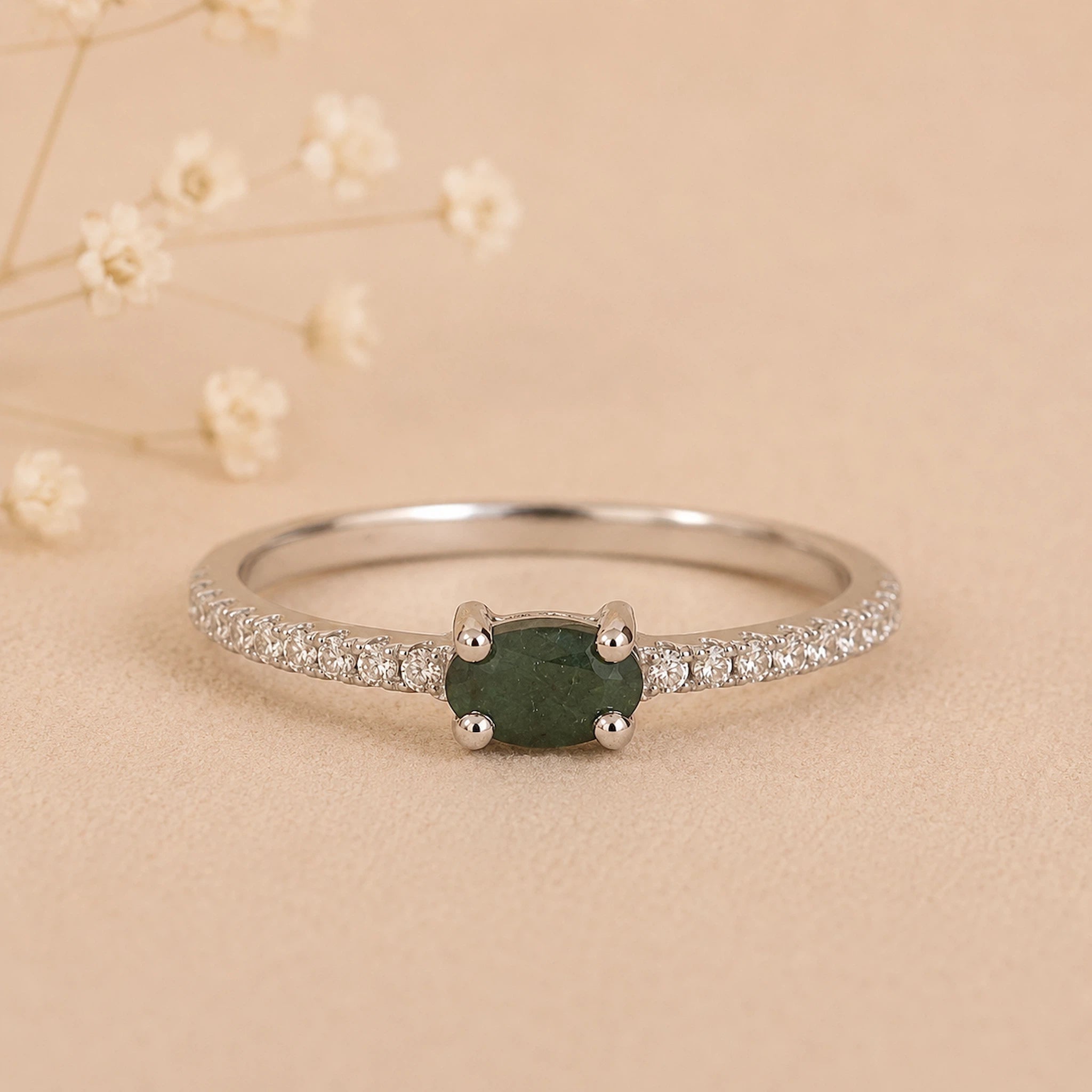 Sterling Silver Pave Ring with a oval shaped green faceted claw set emerald gemstone on a beige background