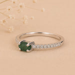 side view of a Sterling Silver Pave Ring with a oval shaped green faceted claw set emerald gemstone on a beige background