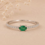 Classic Sterling Silver Pave Stacking ring with a oval faceted claw set emerald gemstone on a beige background.