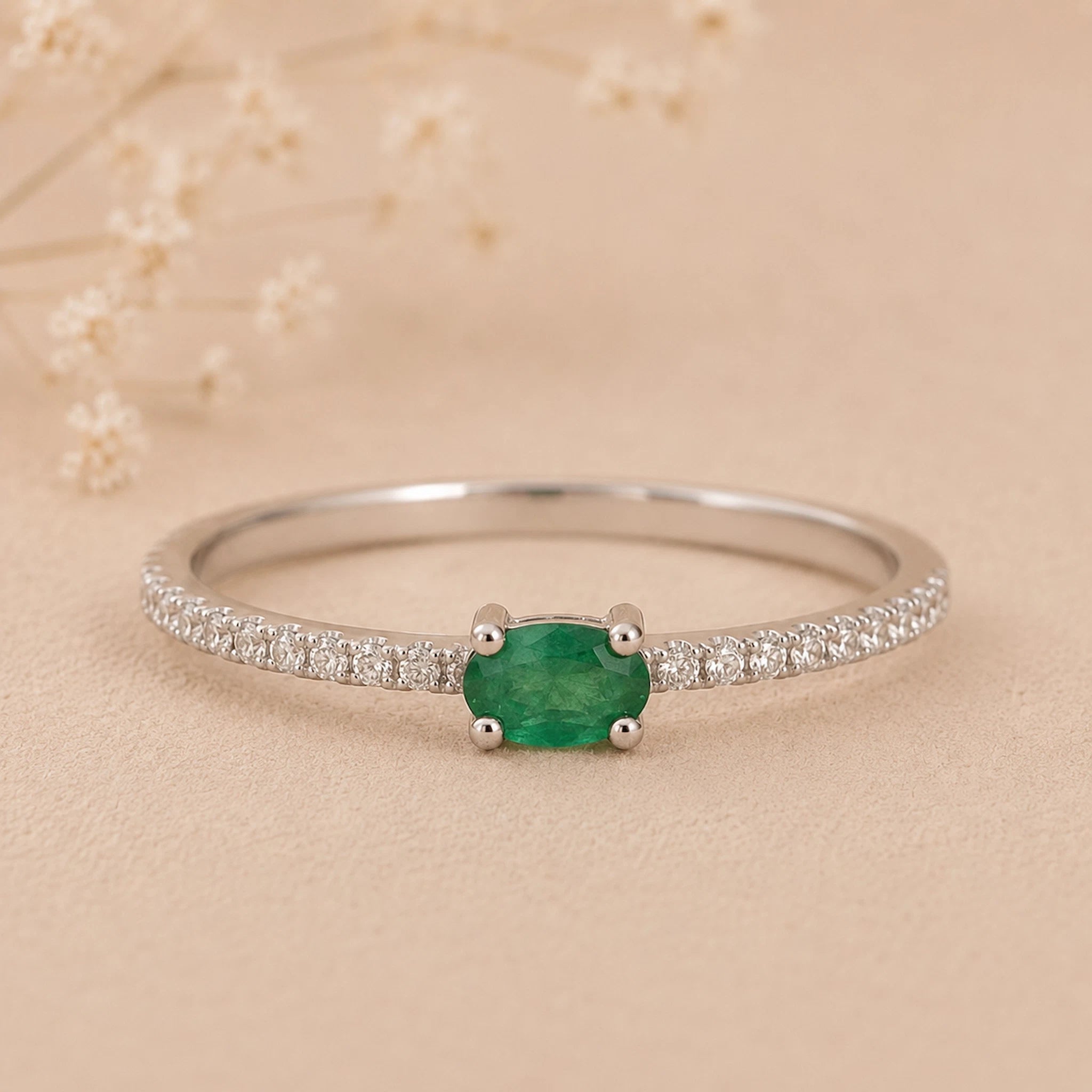 Classic Sterling Silver Pave Stacking ring with a oval faceted claw set emerald gemstone on a beige background.