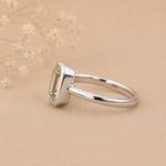 Sterling Silver ring with a emerald-cut, bezel set green amethyst gemstone on a beige background
