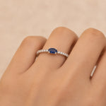 Ring with a blue sapphire gemstone and cubic zirconia accents on a finger against a beige background