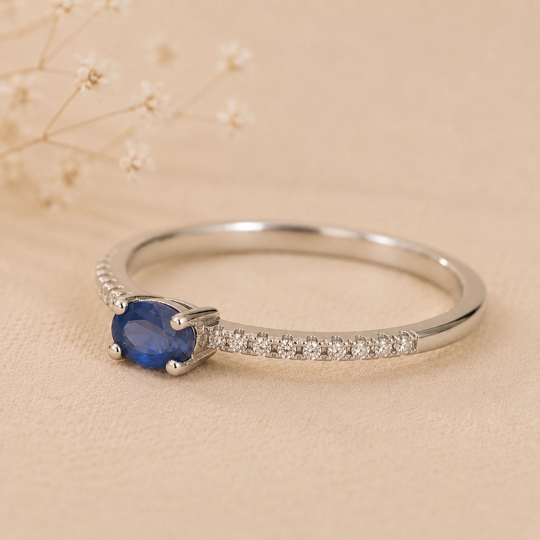 Dainty sterling silver stacking ring featuring a central oval blue sapphire and pavé cubic zirconia accents.