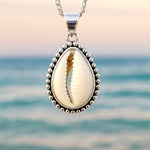 sterling silver cowrie Shell pendant necklace with against a blurred ocean background