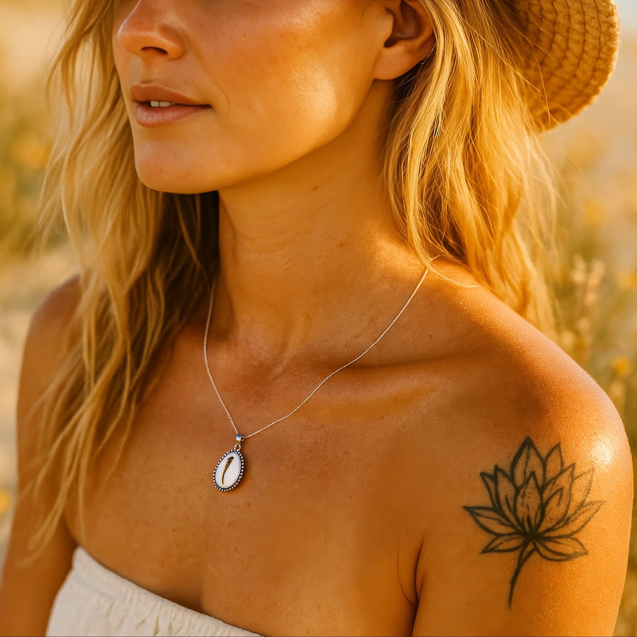 Woman wearing a straw hat and a silver cowrie shell necklace by womens jewellery brand indie and harper