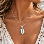 Sterling silver cowrie shell pendant necklace on a fine cable chain, worn with a white lace top