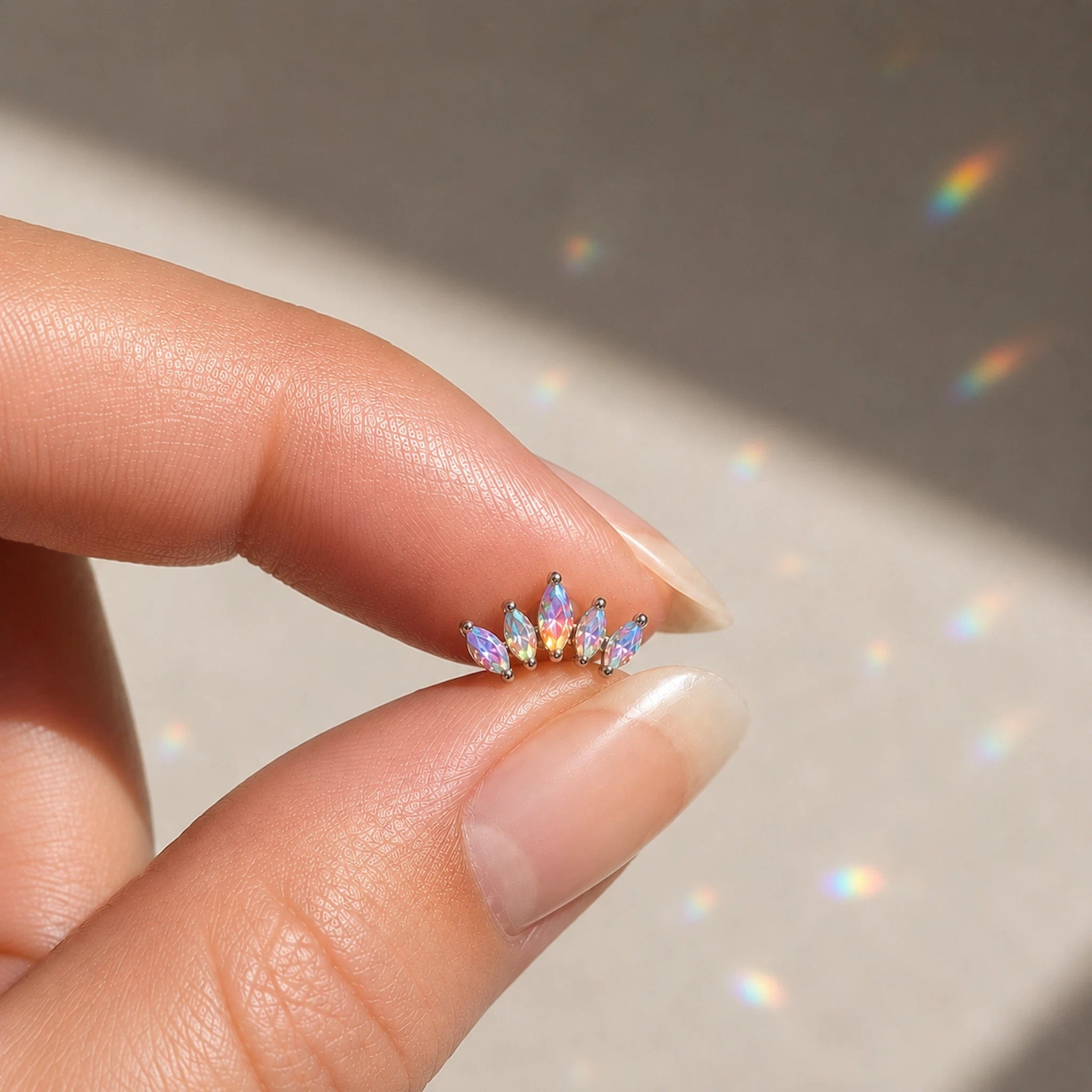 Multicolored gemstone earring held between fingers against a neutral background