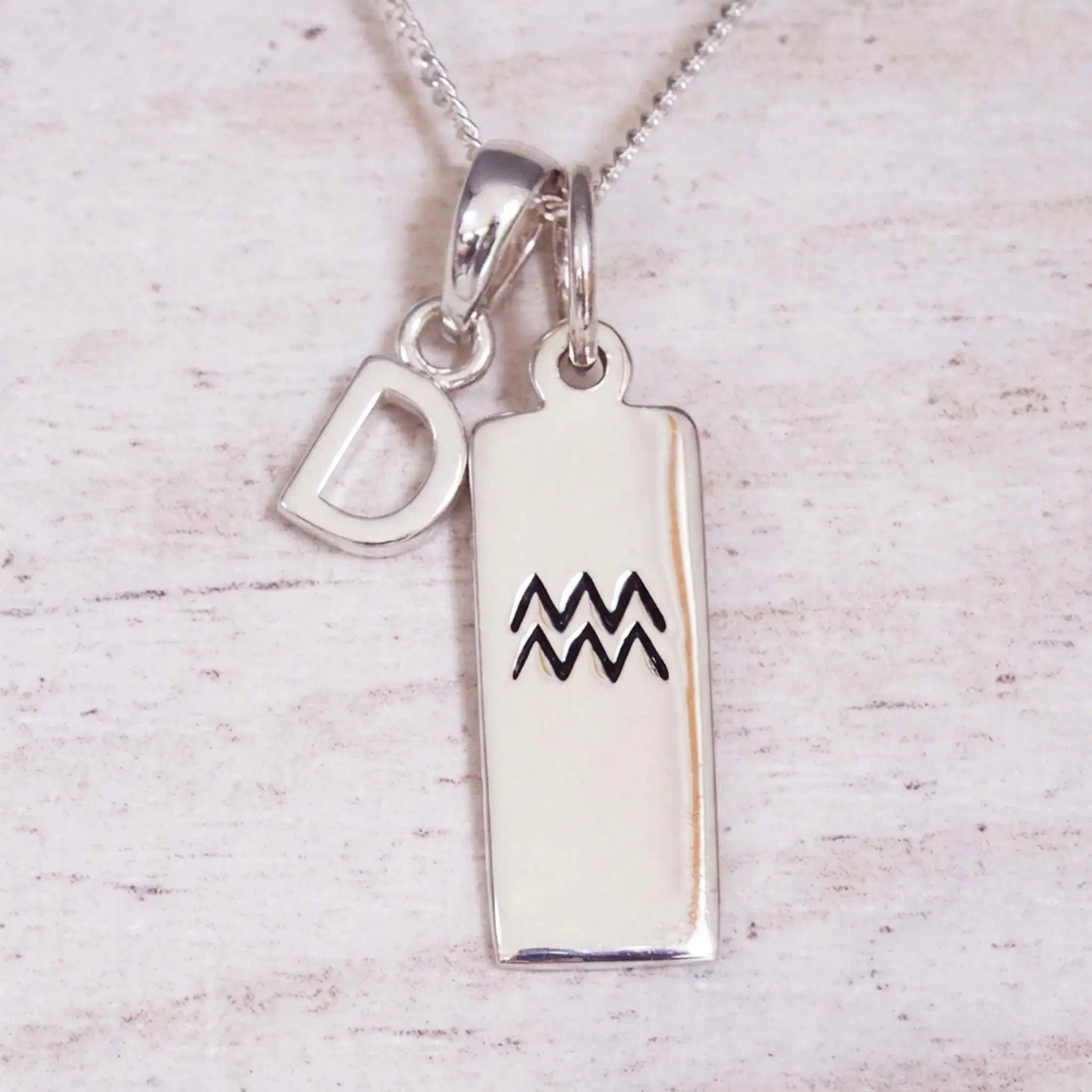 Sterling Silver D Initial and Aquarius Necklace on a fine silver chain against a light wooden background