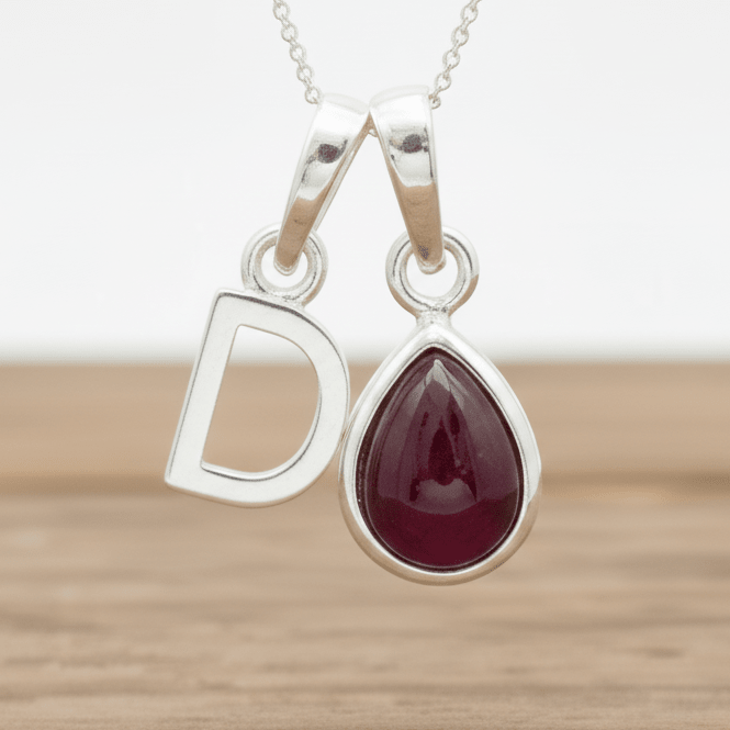 Silver d initial necklace with a teardrop-shaped red ruby gemstone pendant on a wooden surface.