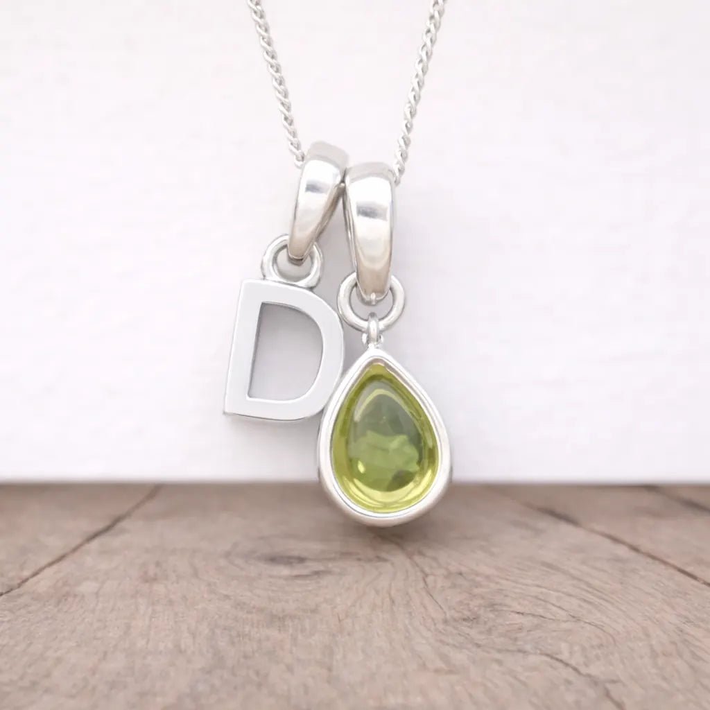 Silver necklace with a 'D' pendant and a teardrop-shaped green gemstone on a wooden surface.