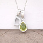 Silver necklace with a 'D' pendant and a teardrop-shaped green gemstone on a wooden surface.