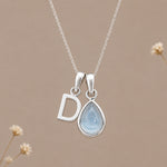 Sterling silver initial D and November natural blue topaz necklace on a taupe background with sparse ivory flowers