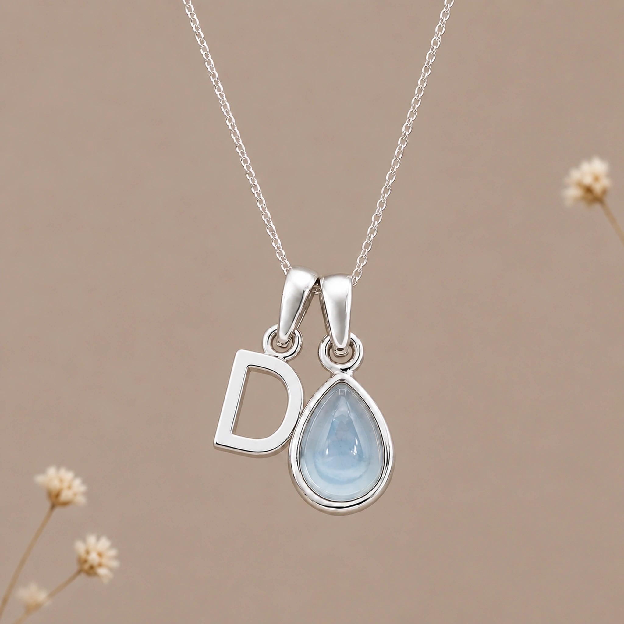 Sterling silver initial D and November natural blue topaz necklace on a taupe background with sparse ivory flowers