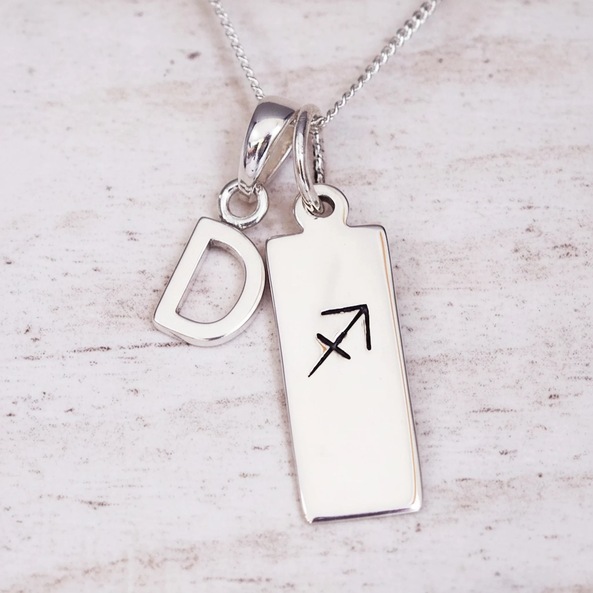 sterling silver necklace with a 'D' initial pendant and a sagittarius zodiac pendant on a light background