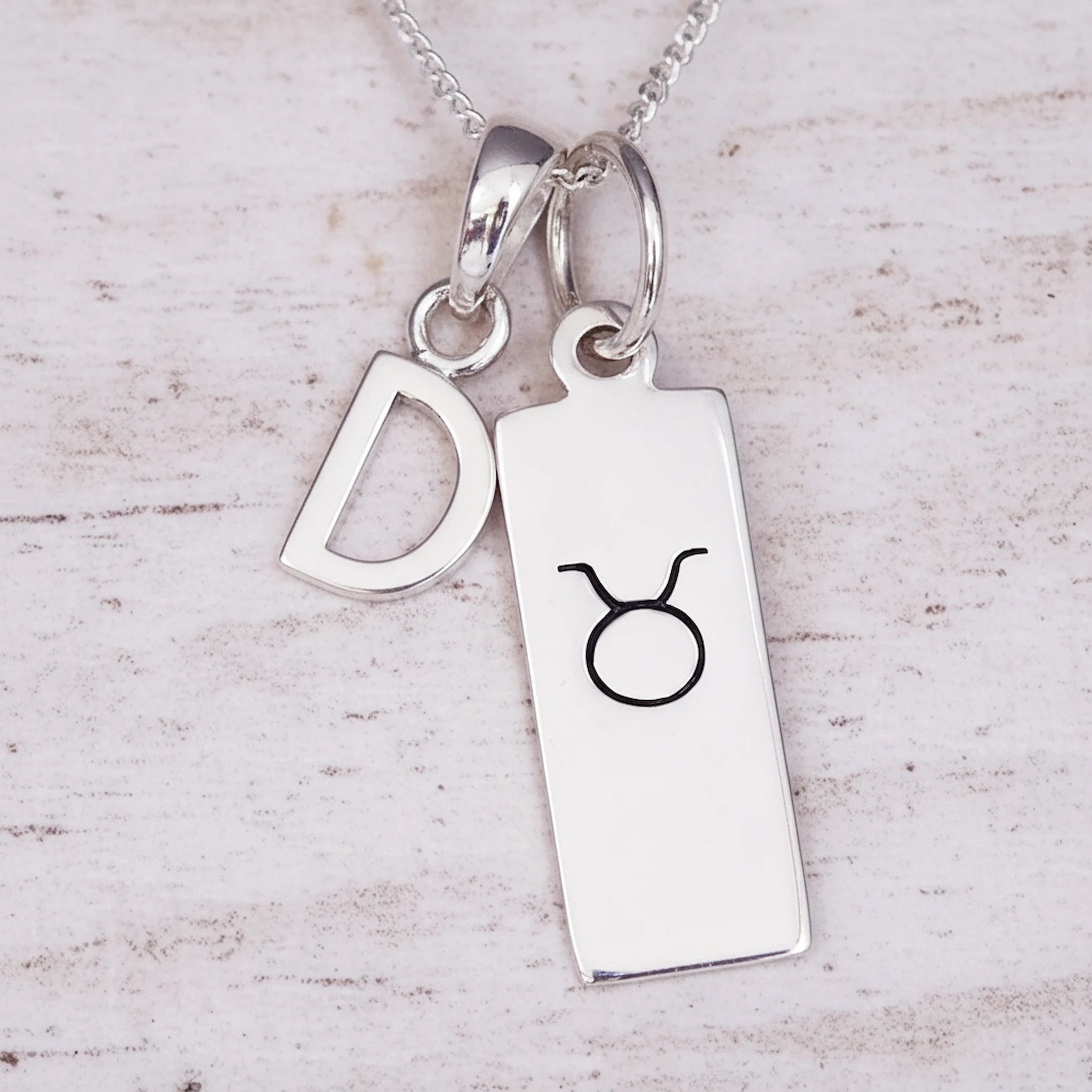 sterling Silver necklace with a 'D' initial pendant and a taurus zodiac star sign pendant on a light wooden background.