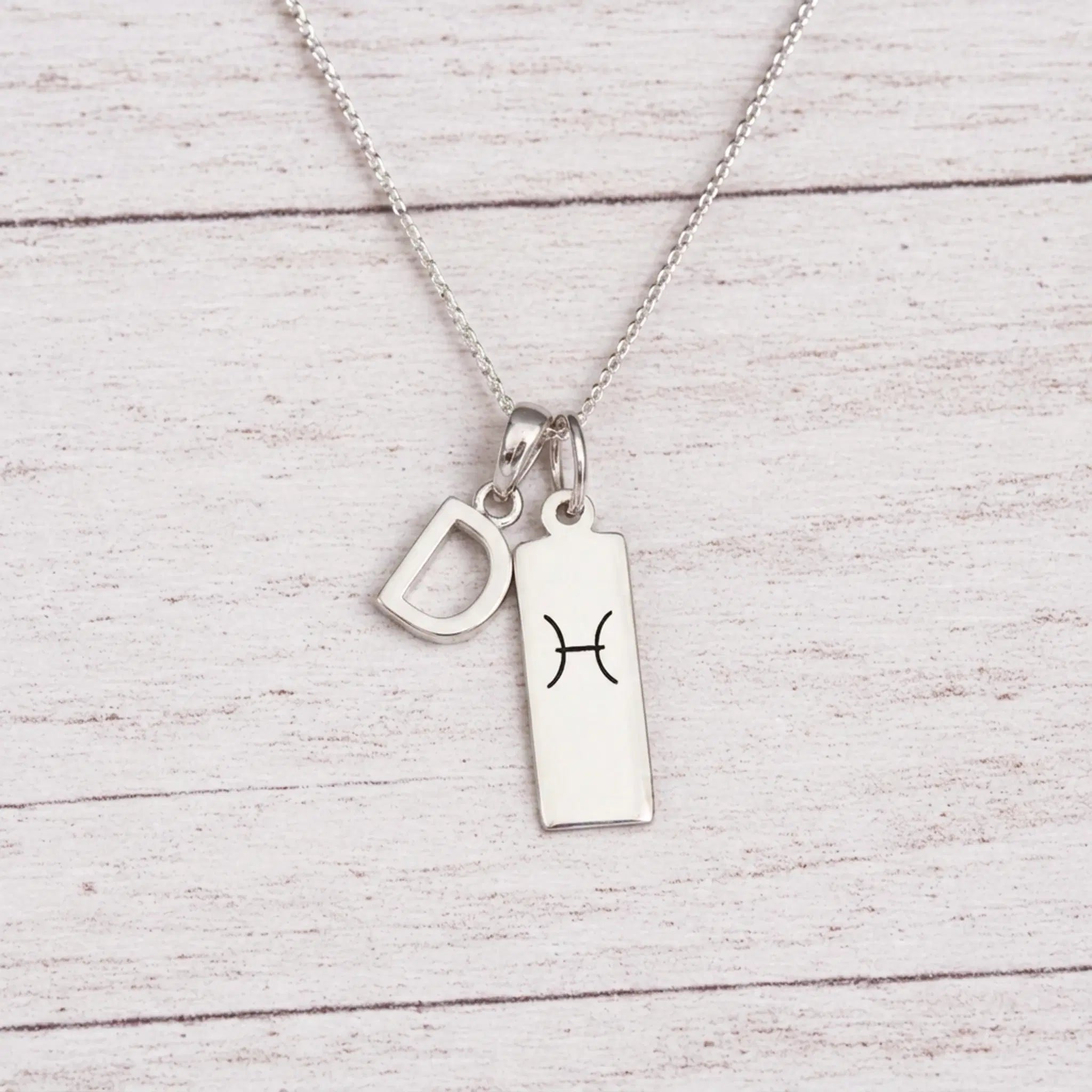 sterling silver D initial Pisces Necklace on a fine silver chain against a light wooden background