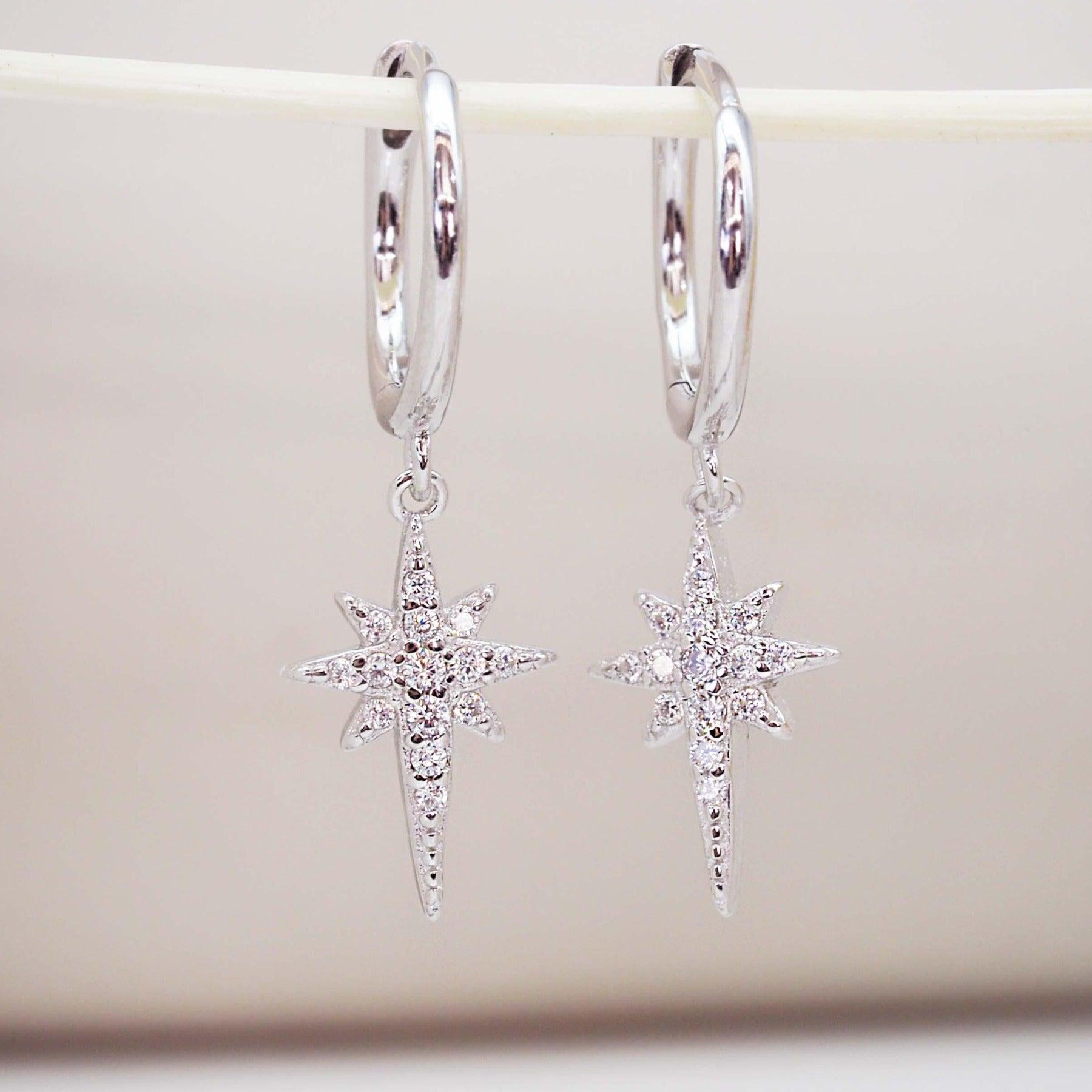 Silver star-shaped hoop earrings with cubic zirconias on a white background