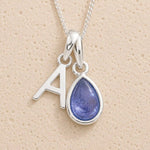 Sterling Silver december birthstone necklace with a teardrop-shaped blue tanzanite gemstone pendant and letter 'A' charm on a beige background.