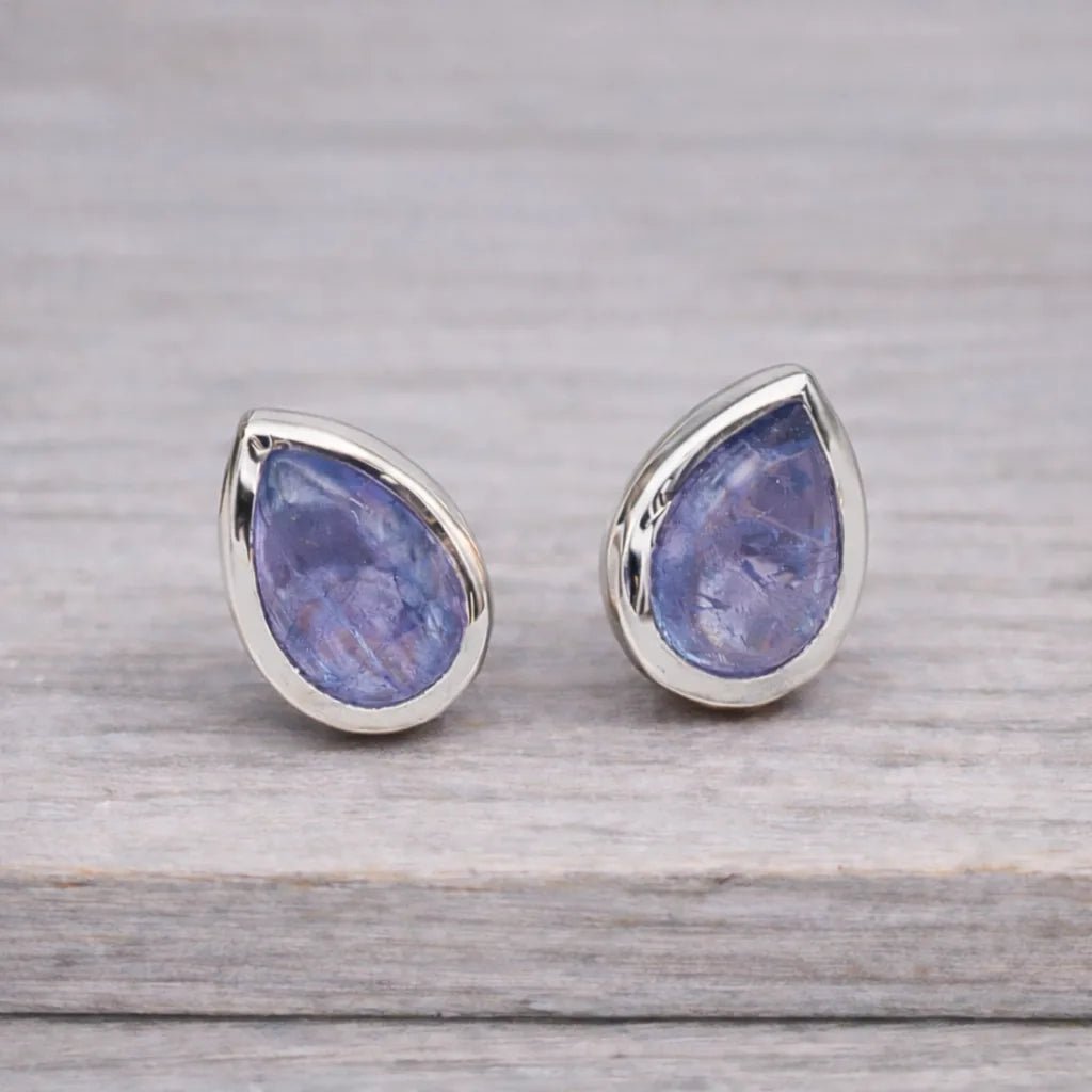 Teardrop-shaped tanzanite gemstone stud earrings with sterling silver settings on a wooden surface