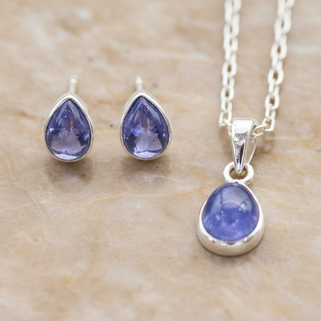 Teardrop-shaped blue tanzanite gemstone jewellery set with sterling silver necklace and stud earrings on a stone surface
