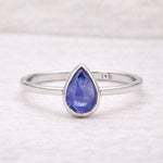 Silver ring with a teardrop-shaped natural tanzanite blue gemstone on a white background