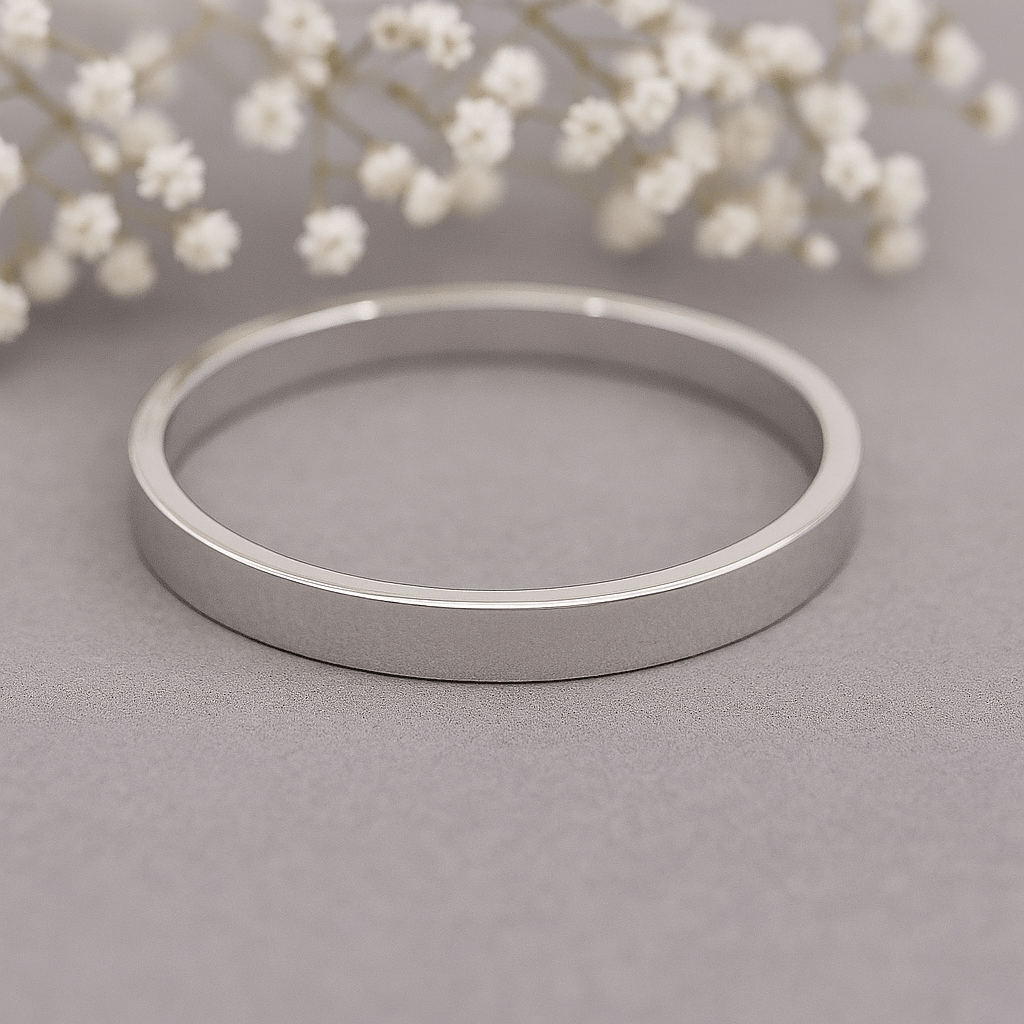 Silver band ring on a grey surface with white flowers in the background 