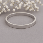 Silver band ring on a grey surface with white flowers in the background 