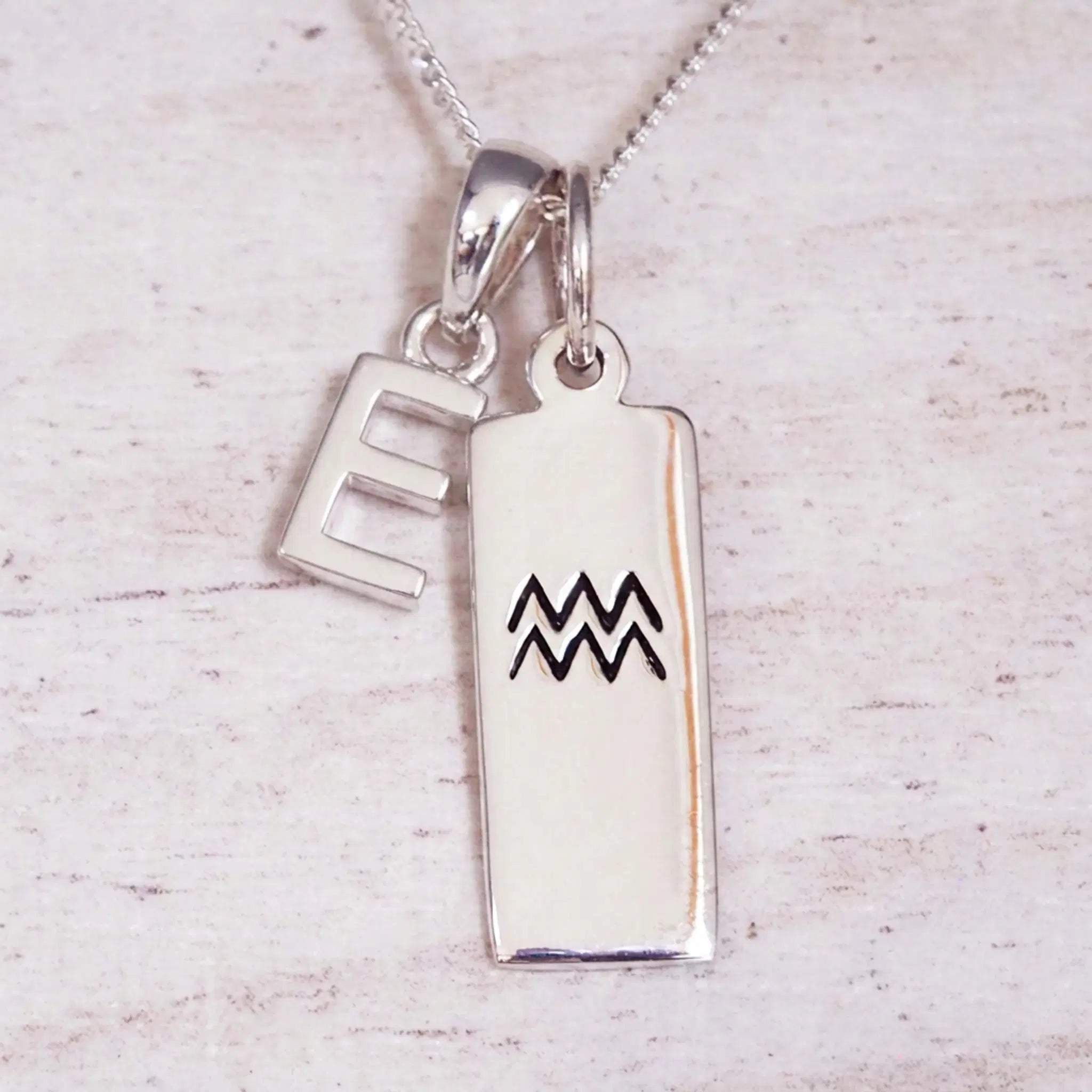 Sterling Silver E Initial and Aquarius Necklace on a fine silver chain against a light wooden background