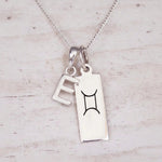 Sterling silver E initial and GeminI Necklace on a fine silver chain on a light wooden background