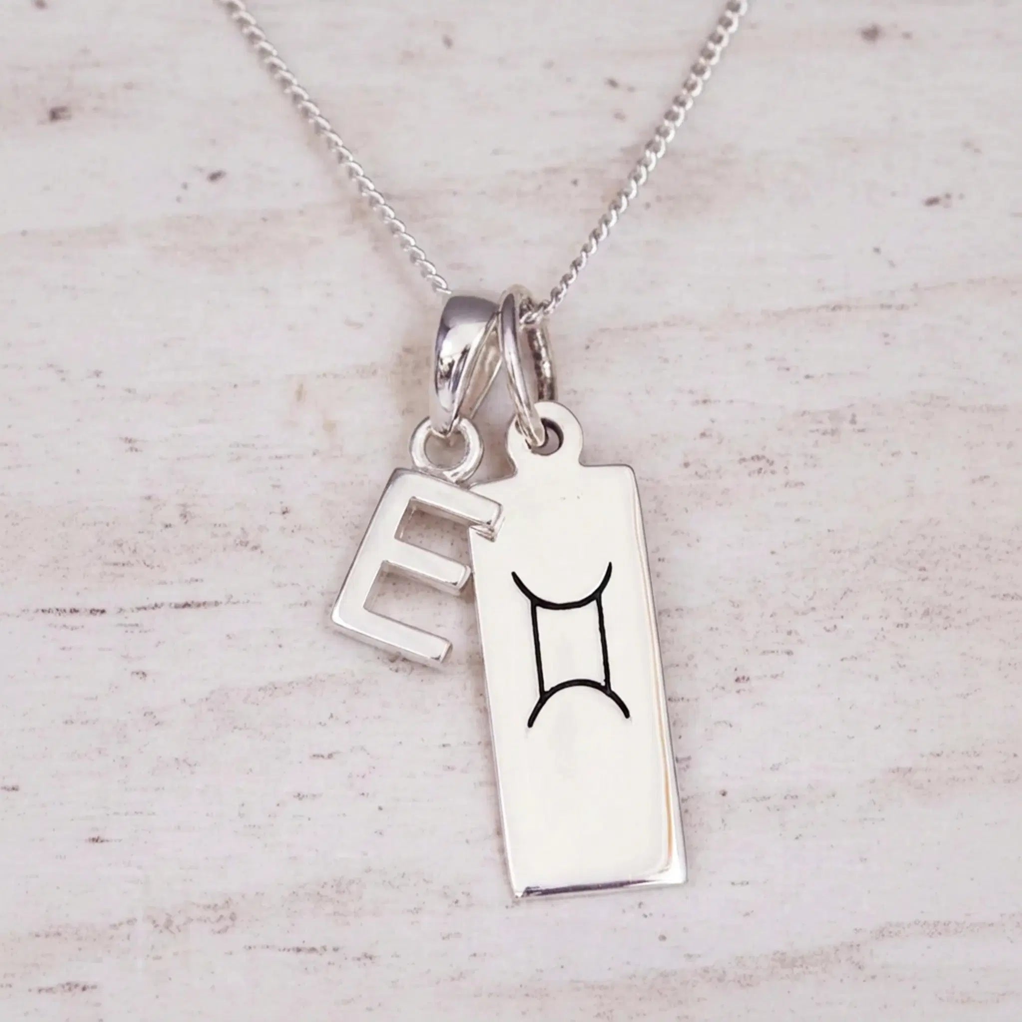 Sterling silver E initial and GeminI Necklace on a fine silver chain on a light wooden background