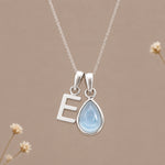 Sterling silver initial E and November natural blue topaz necklace on a taupe background with sparse ivory flowers