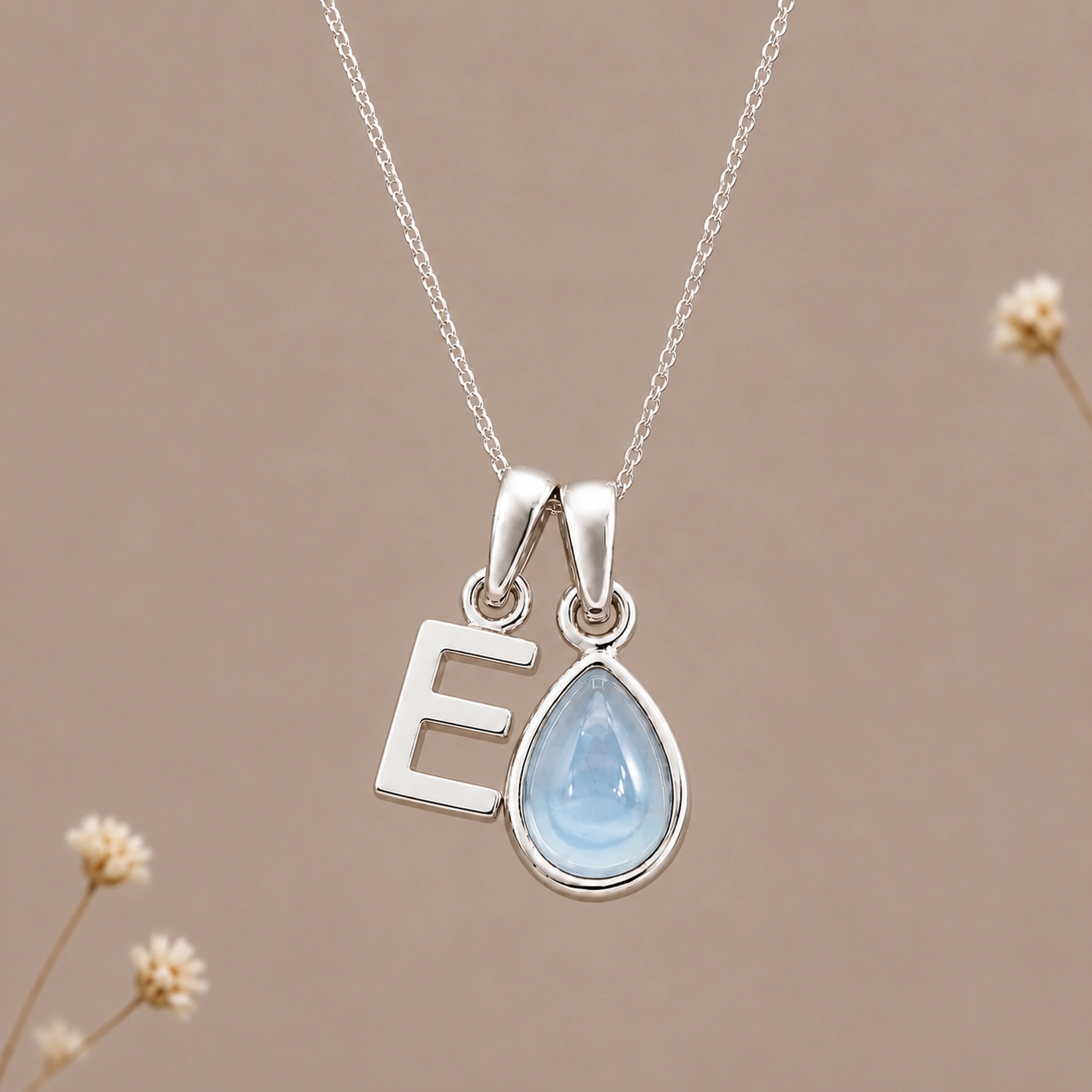Sterling silver initial E and November natural blue topaz necklace on a taupe background with sparse ivory flowers