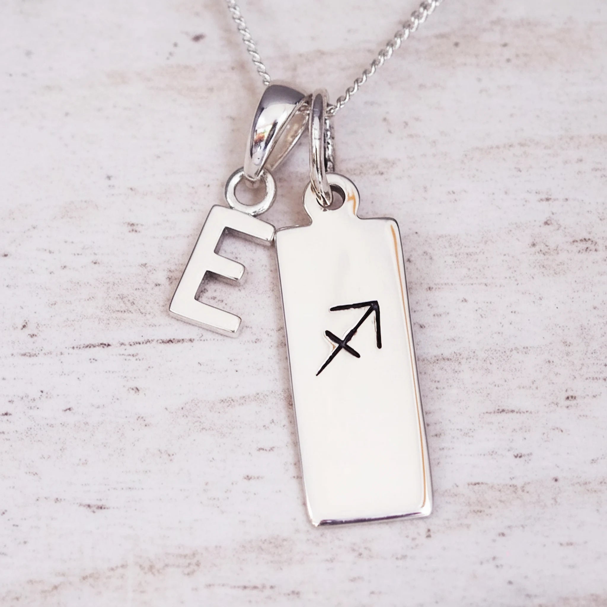 sterling silver necklace with a 'E' initial pendant and a sagittarius zodiac pendant on a light background