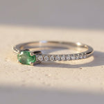 Silver ring with a green gemstone and small diamonds on a textured surface