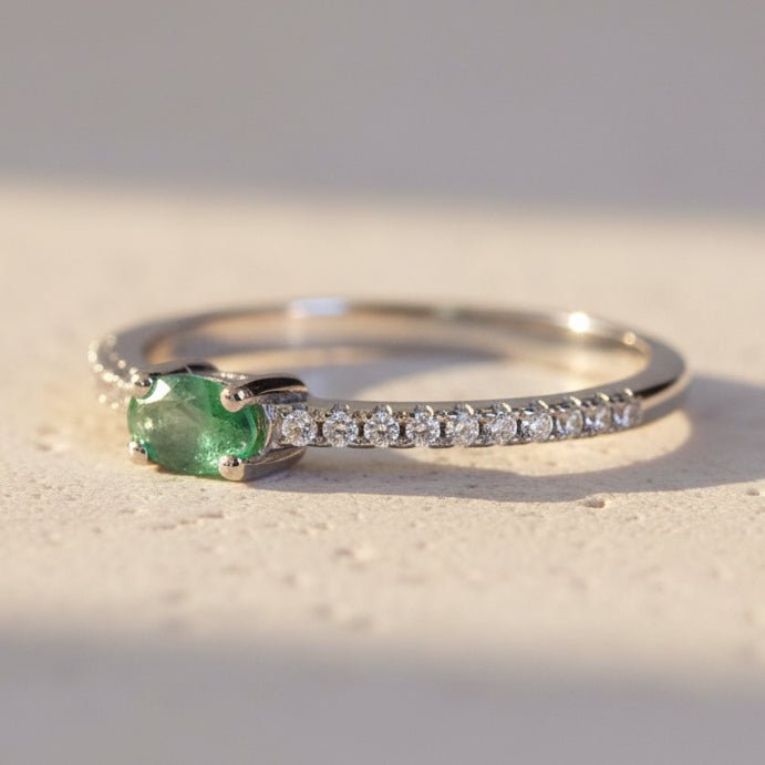 Silver ring with a green gemstone and small diamonds on a textured surface