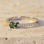 Silver ring with a green gemstone and small diamonds on a textured beige background