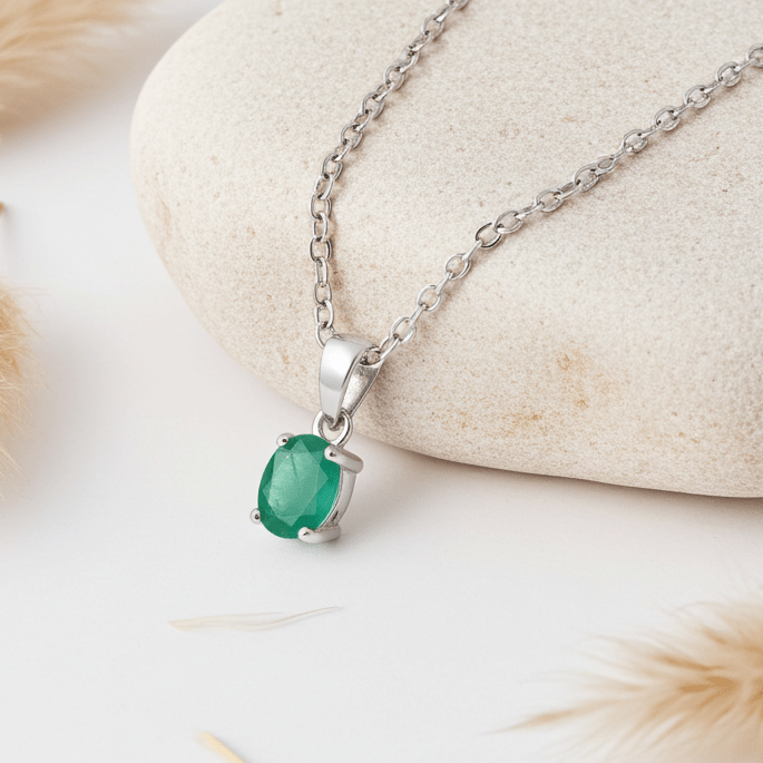Silver necklace with a green gemstone pendant on a stone surface