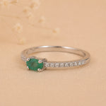 side view of a Sterling Silver Pave Ring with a oval shaped green faceted claw set emerald gemstone on a beige background