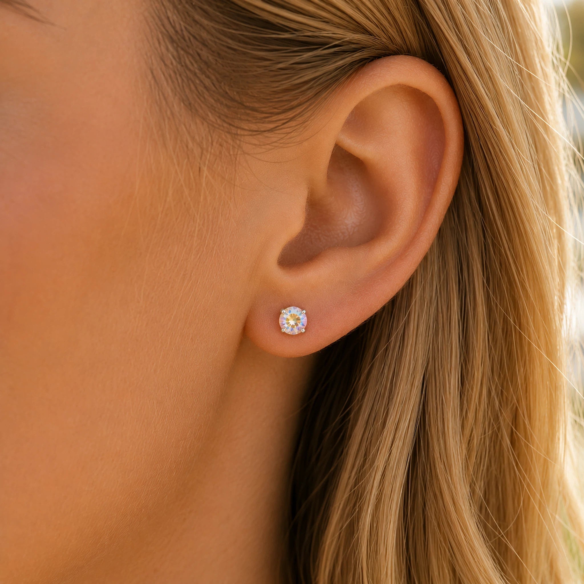 A close-up of a person's ear wearing a small round stud earring with a clear gemstone in a gold setting.