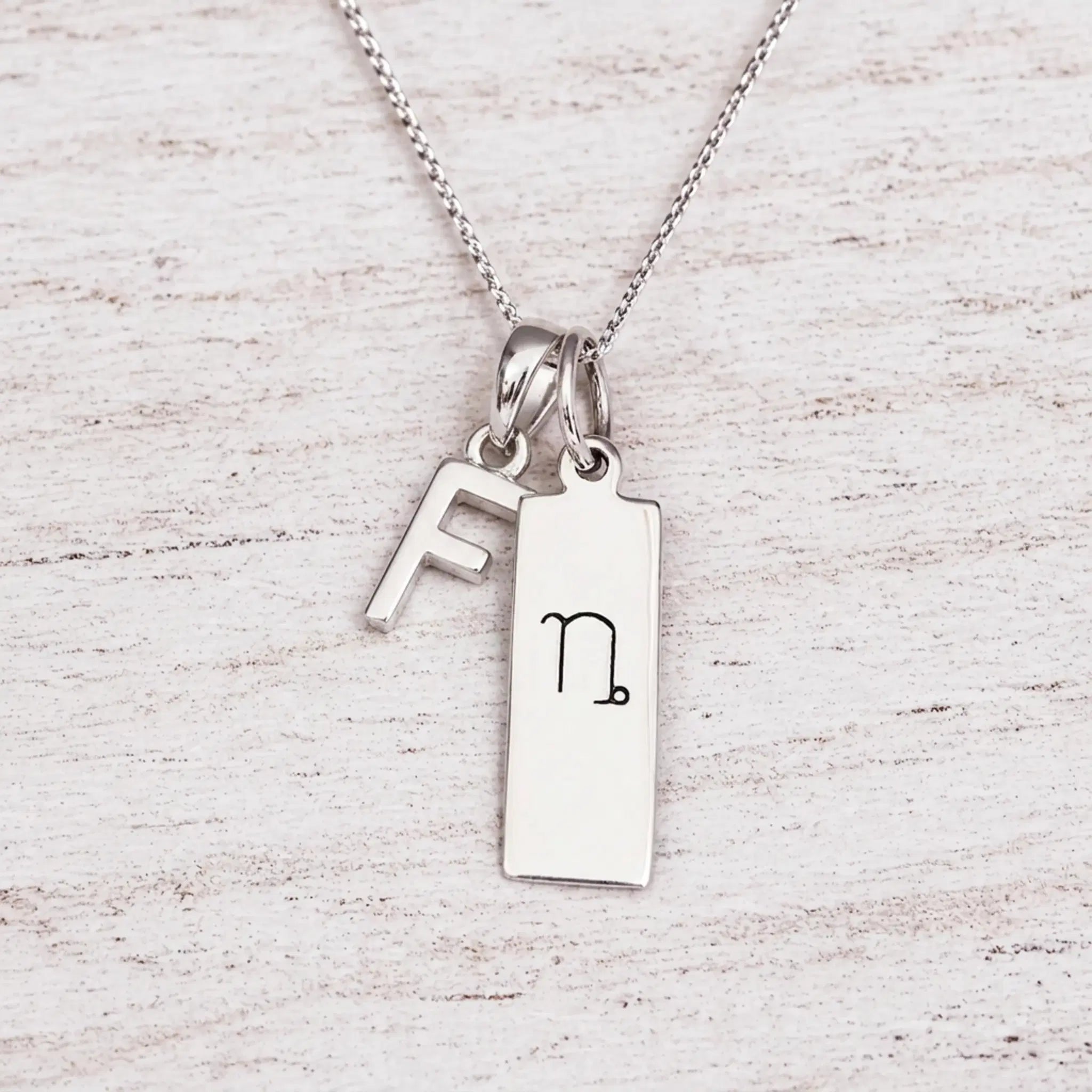 sterling silver initial F pendant and capricorn necklace on a fine silver chain against a light wooden background