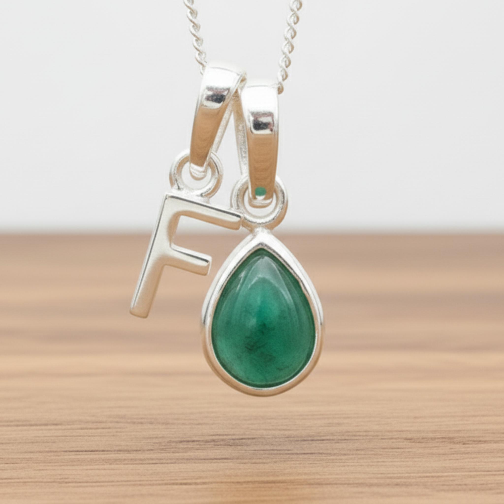 Silver Initial F necklace with a teardrop-shaped Emerald gemstone pendant hanging above a rustic wooden surface
