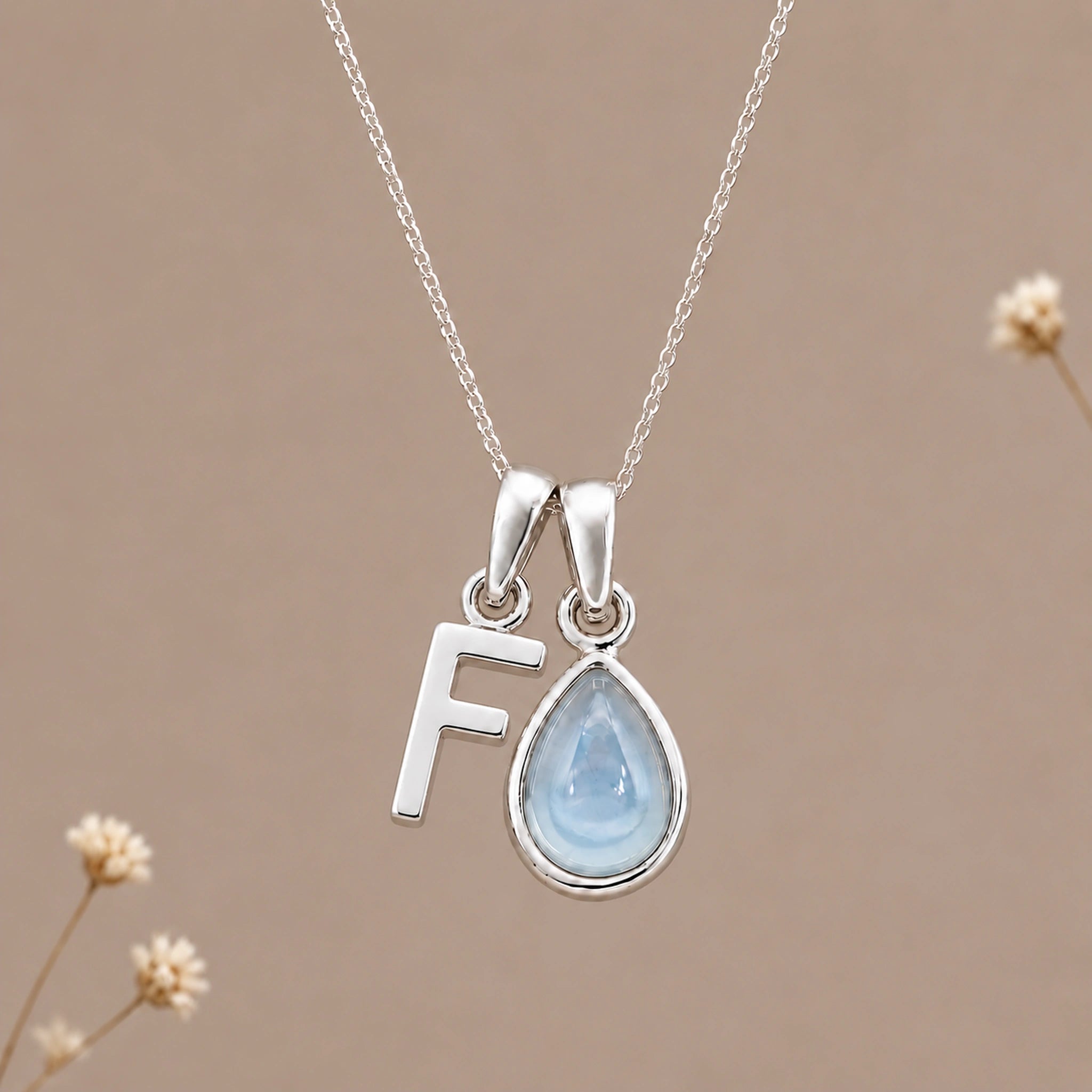 Sterling silver initial F and November natural blue topaz necklace on a taupe background with sparse ivory flowers