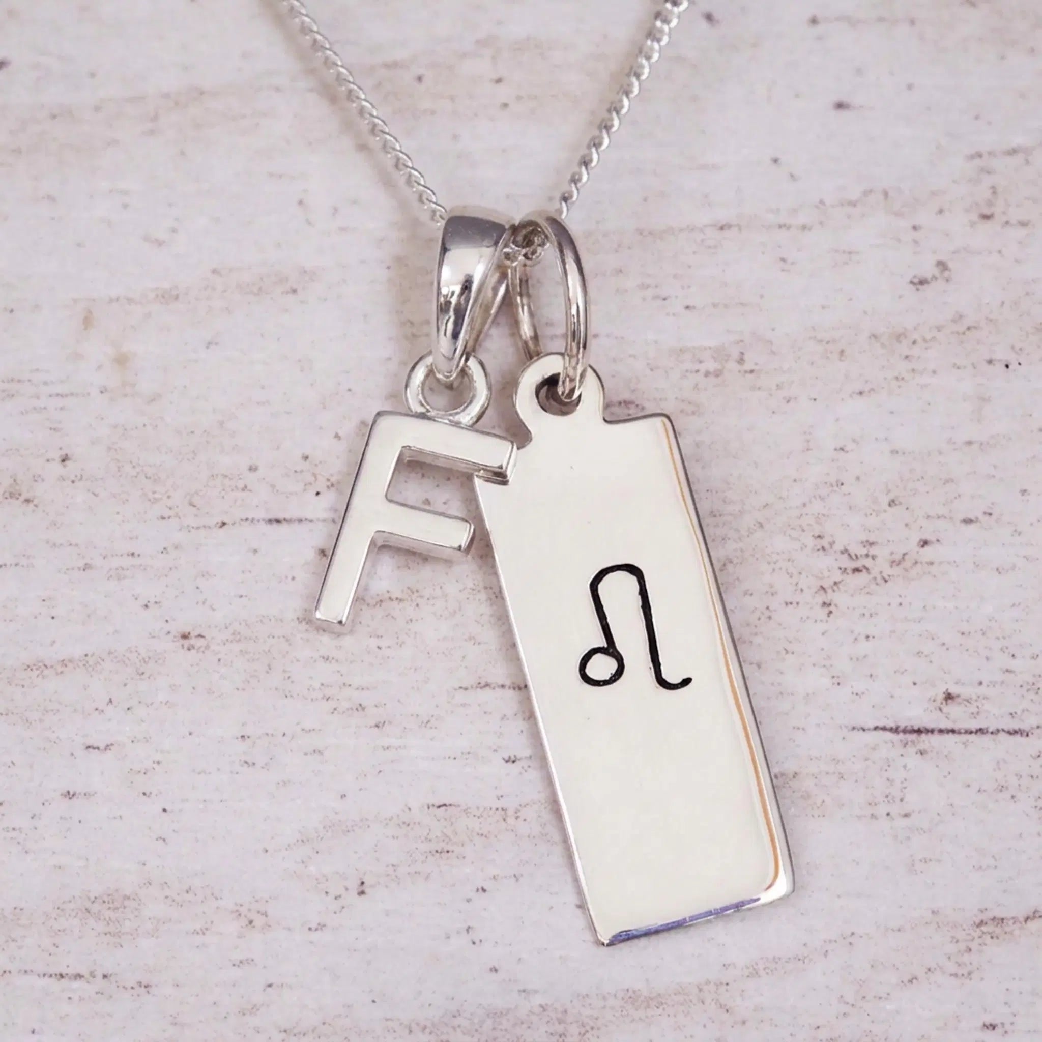 sterling silver initial f leo zodiac star sign pendant necklace against a light wooden background